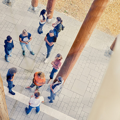 Blick von oben auf eine Menschengruppe, die locker verteilt im äußeren Eingangsbereich des NAWAREUMs steht.